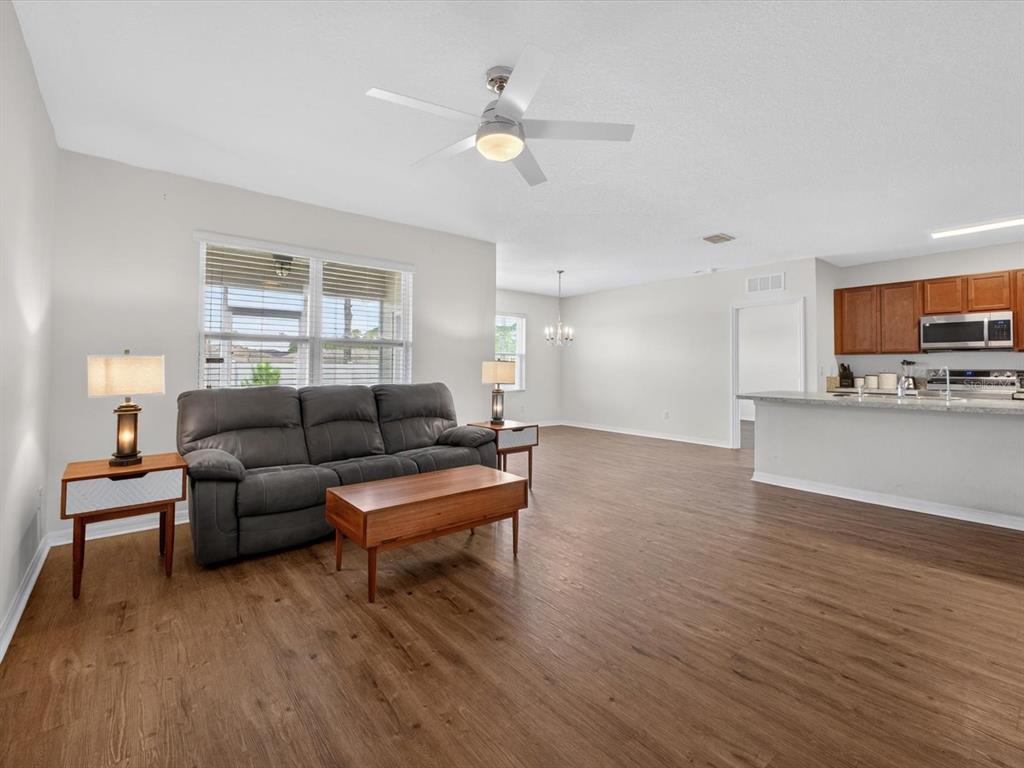 A living room with wood-look flooring, a gray sofa, and an adjacent open kitchen — 16701 BROADFORD LANE, CLERMONT, FL