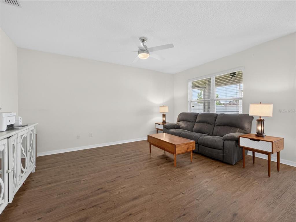 A living room features wood-look flooring, a gray sofa, a coffee table, and a ceiling fan — 16701 BROADFORD LANE, CLERMONT, FL