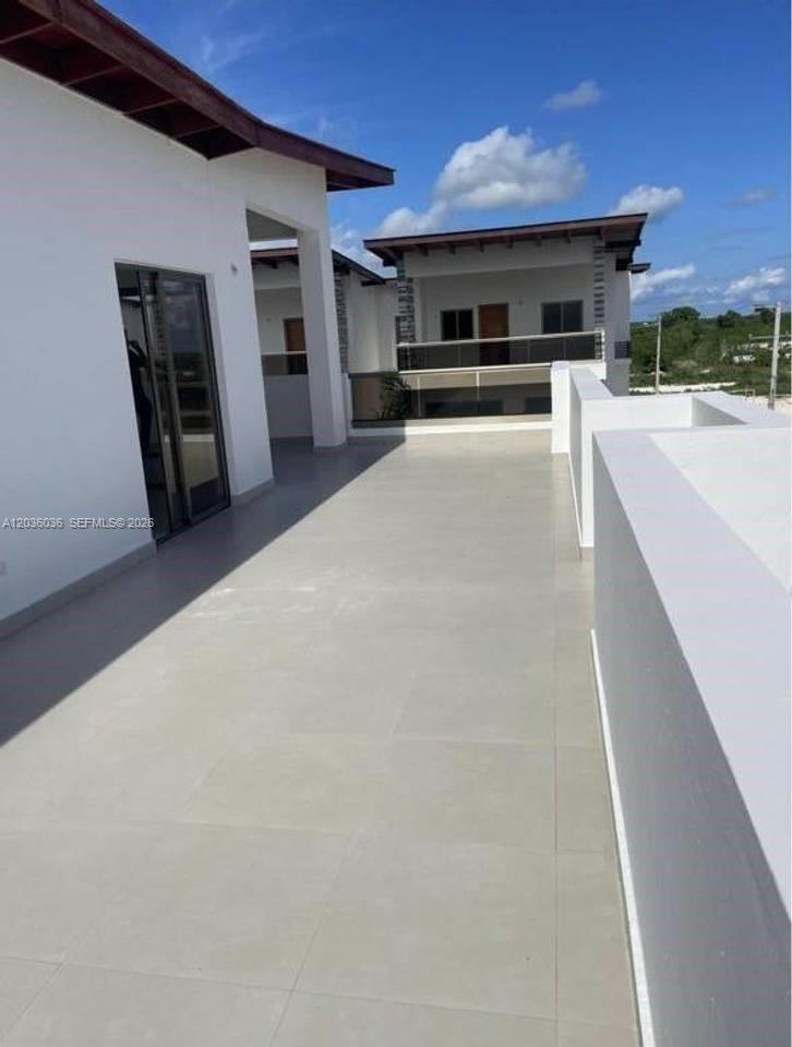A spacious, light-colored tiled balcony connects two modern white buildings under a blue sky — 0 Cap cana # 0, FL