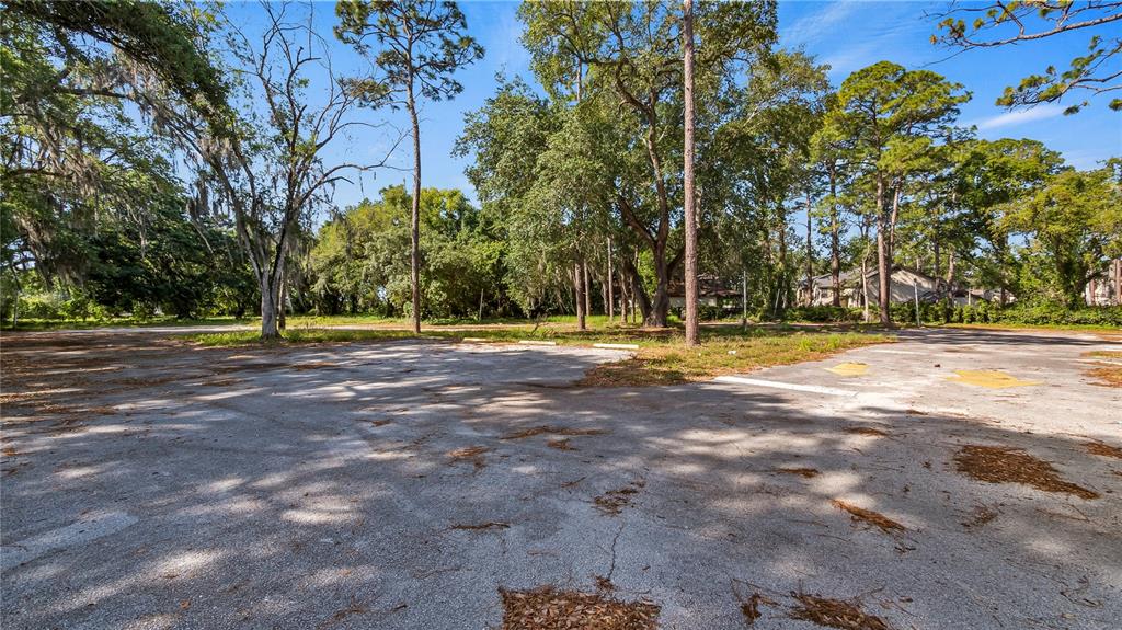 An empty, weathered asphalt parking lot is surrounded by tall trees under a blue sky — 1500 N HOAGLAND BOULEVARD, KISSIMMEE, FL