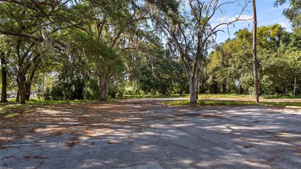 A paved parking lot is surrounded by large trees with hanging Spanish moss — 1500 N HOAGLAND BOULEVARD, KISSIMMEE, FL