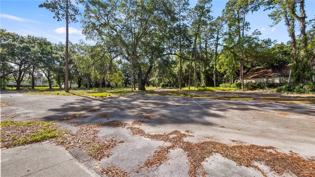 An empty, weathered asphalt parking lot is surrounded by mature trees and a small building — 1500 N HOAGLAND BOULEVARD, KISSIMMEE, FL
