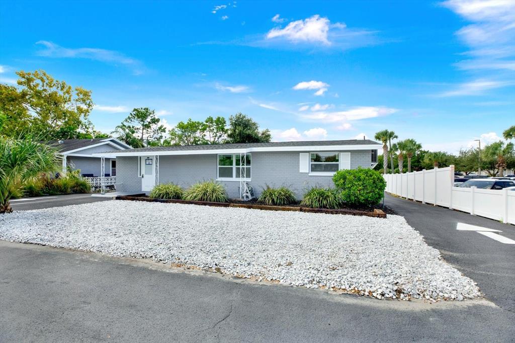 A gray, single-story house features a white gravel front yard and a white vinyl fence — 6102 INDIANA AVENUE, NEW PORT RICHEY, FL