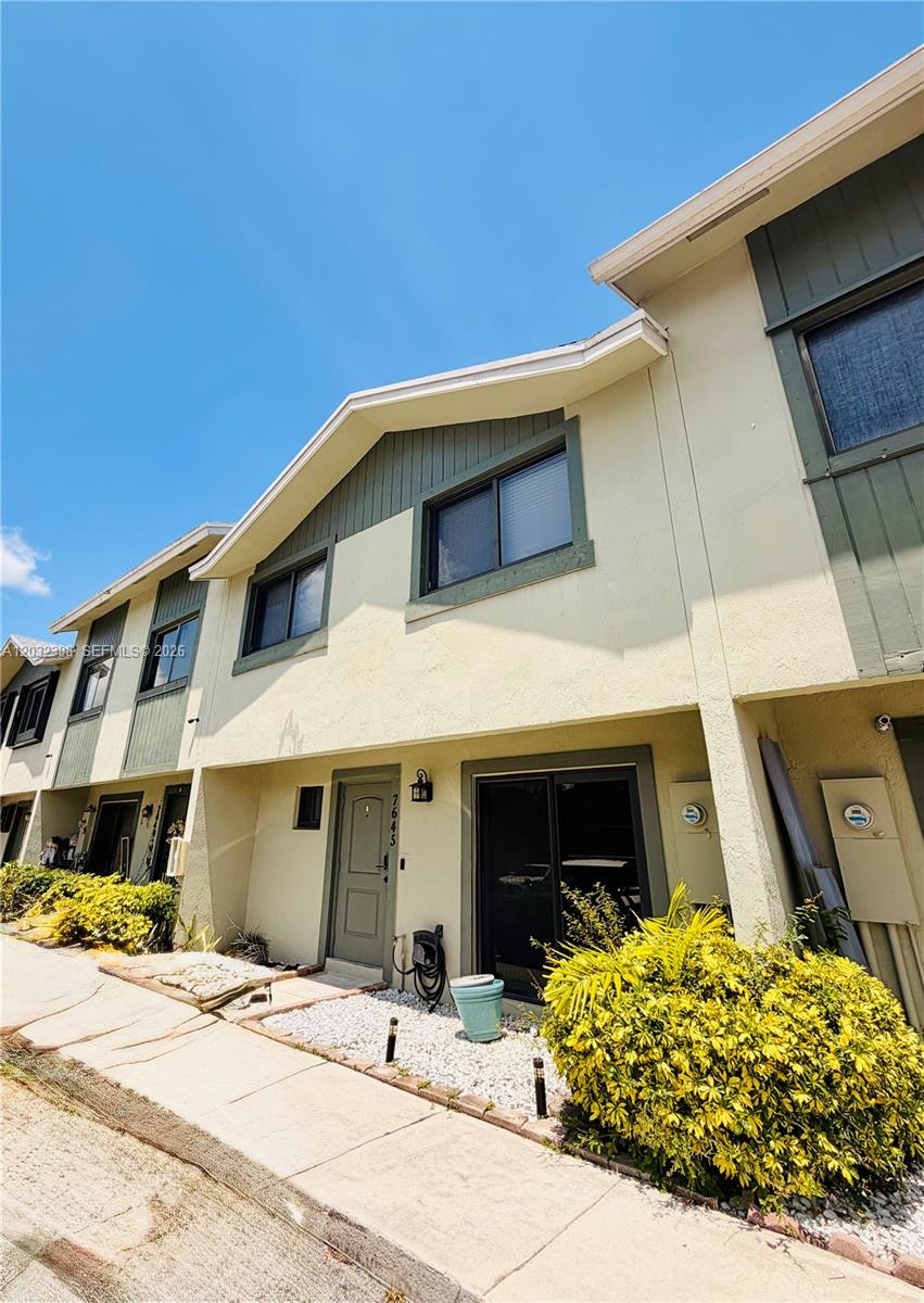 A two-story townhouse exterior features beige stucco walls, dark green trim, and a front entrance — 7645 NW 38th Ct, Sunrise FL 33351, SUNRISE, FL