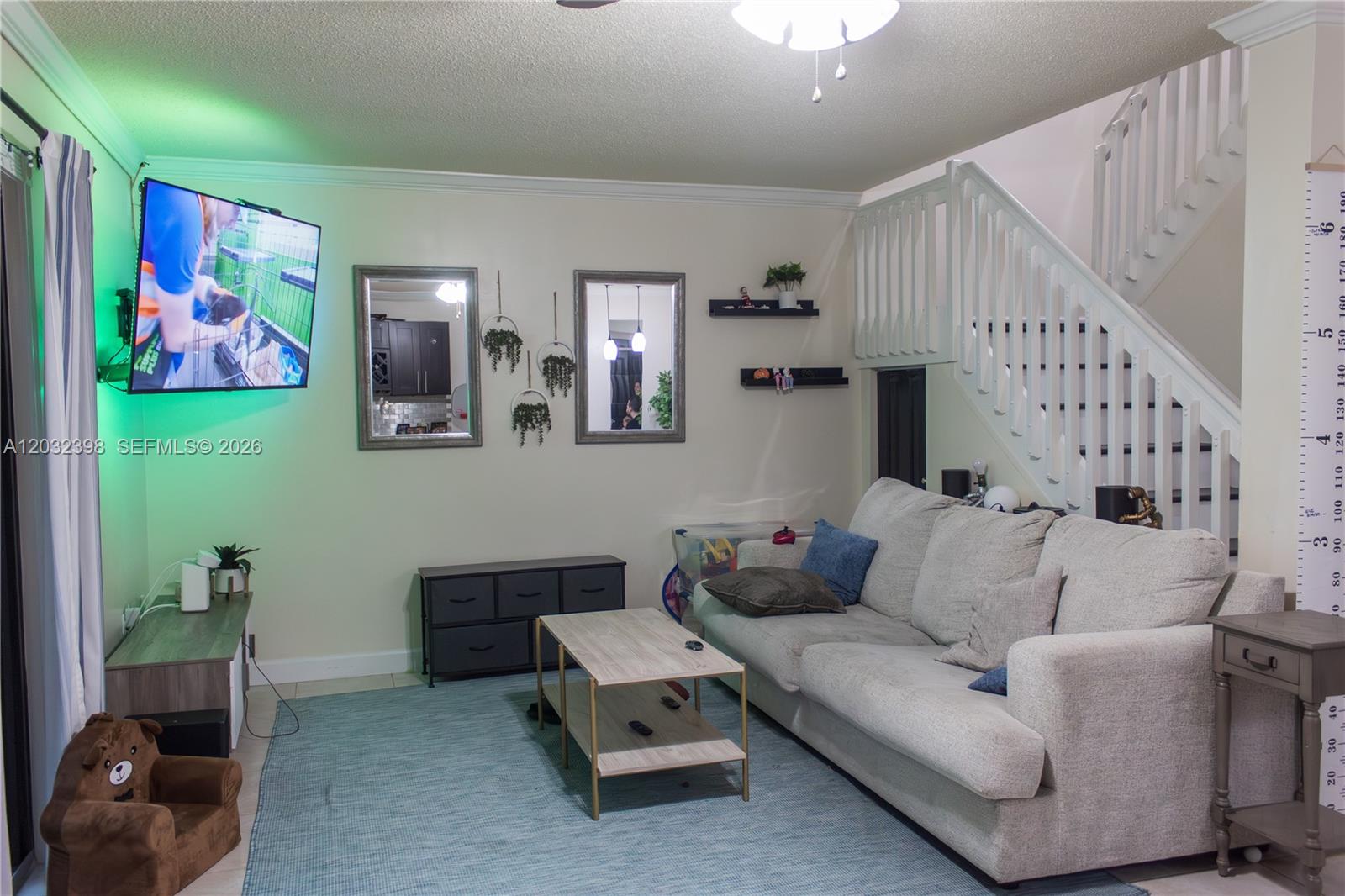A living room features a mounted television, a light-colored sofa, and stairs with white railings — 7645 NW 38th Ct, Sunrise FL 33351, SUNRISE, FL