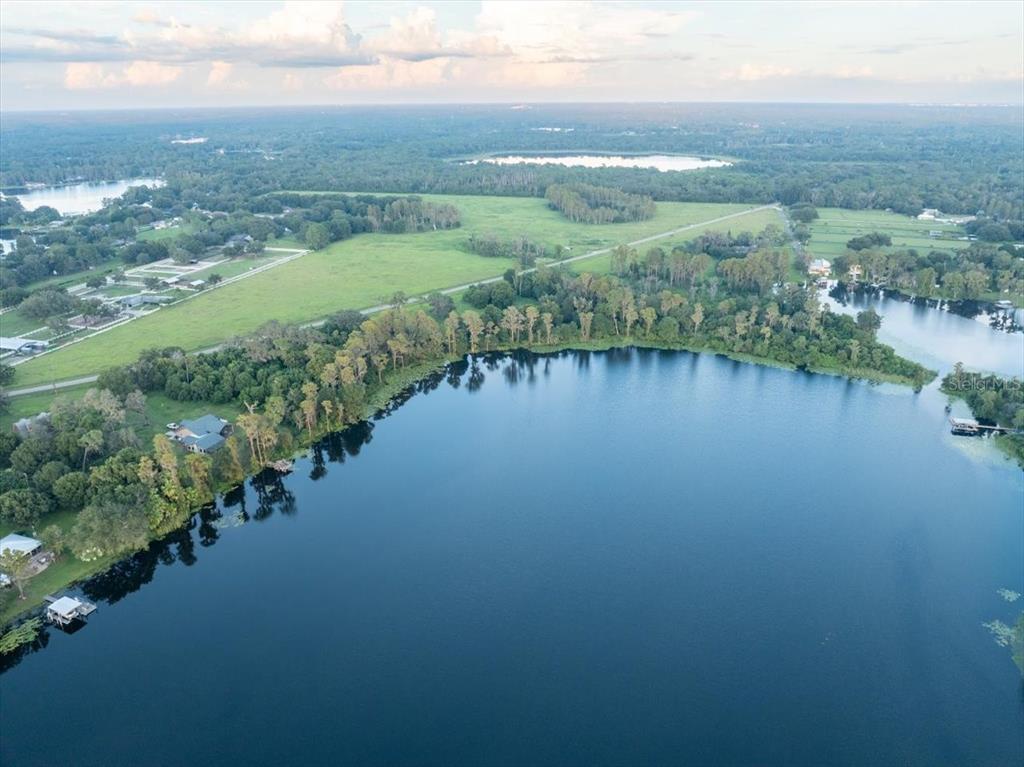 An aerial view shows a large lake surrounded by trees, grassy fields, and residential properties — 16405 BOY SCOUT ROAD, ODESSA, FL