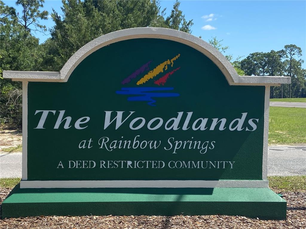 A green sign for The Woodlands at Rainbow Springs stands outdoors in a wooded area — Lot 28 SW 206 CIRCLE, DUNNELLON, FL