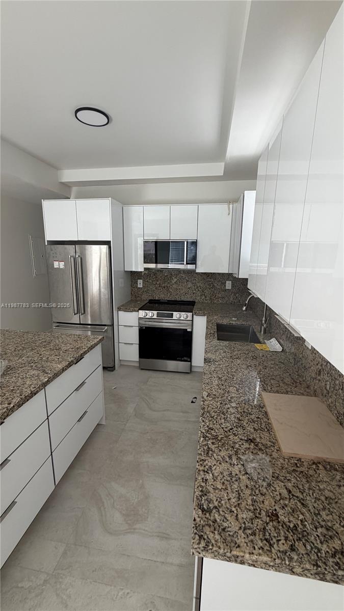 A modern kitchen features white cabinets, granite countertops, and stainless steel appliances — 102 PL SW 18340, Perrine FL 33157, PERRINE, FL
