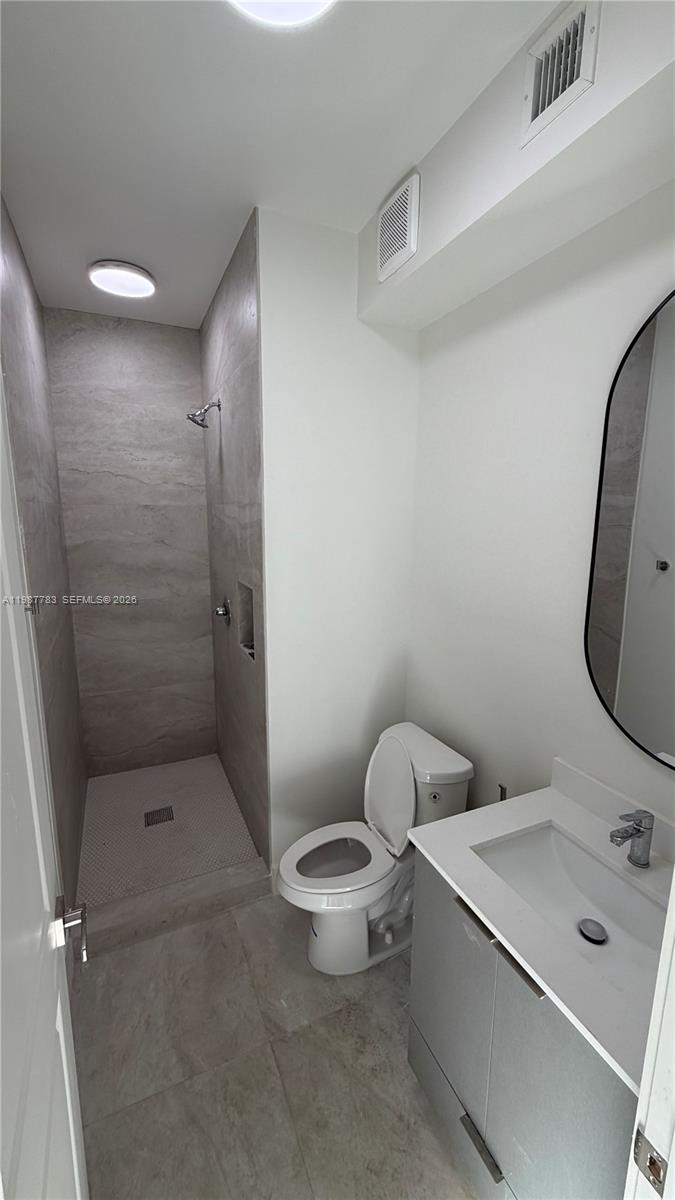 A modern bathroom features a walk-in tiled shower, a white toilet, and a vanity sink — 102 PL SW 18340, Perrine FL 33157, PERRINE, FL