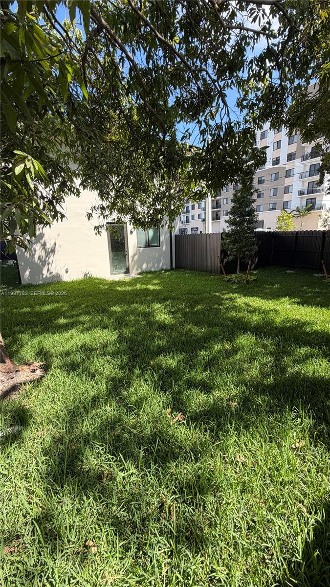 A grassy backyard features a light-colored exterior wall with a door and a dark fence — 102 PL SW 18340, Perrine FL 33157, PERRINE, FL
