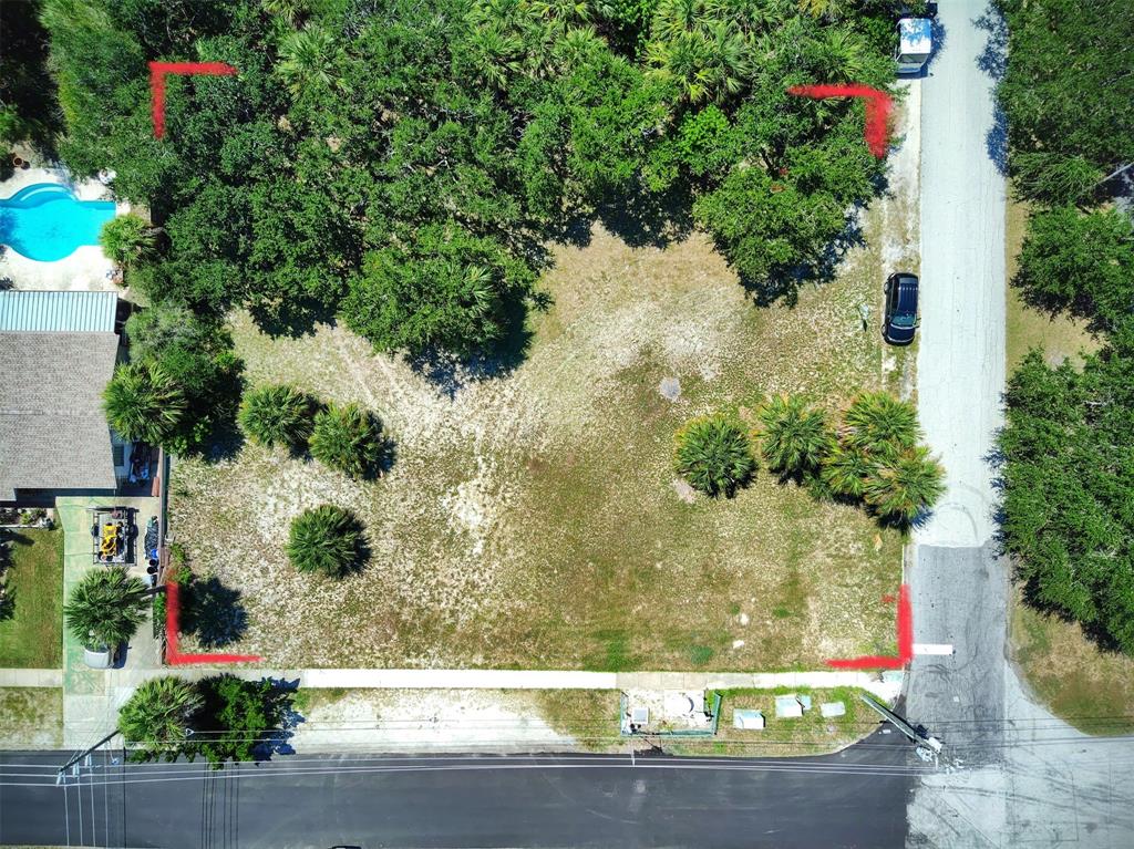 An aerial view shows a vacant, grassy residential lot bordered by trees and a paved road — 102 DESOTO DRIVE, NEW SMYRNA BEACH, FL
