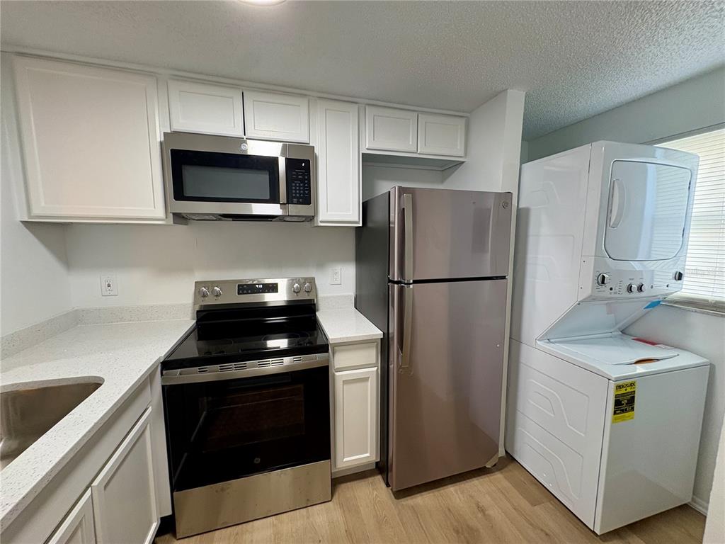A kitchen featuring white cabinets, stainless steel appliances, a refrigerator, and a stacked laundry unit — 308 57TH AVENUE DRIVE E UNIT A, BRADENTON, FL