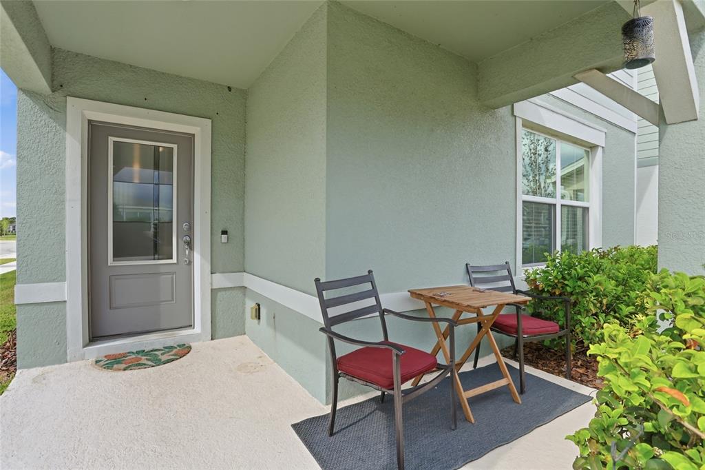 A covered porch features a gray door, two chairs, and a small table on a rug — 1818 GROVELINE ROAD, ST CLOUD, FL