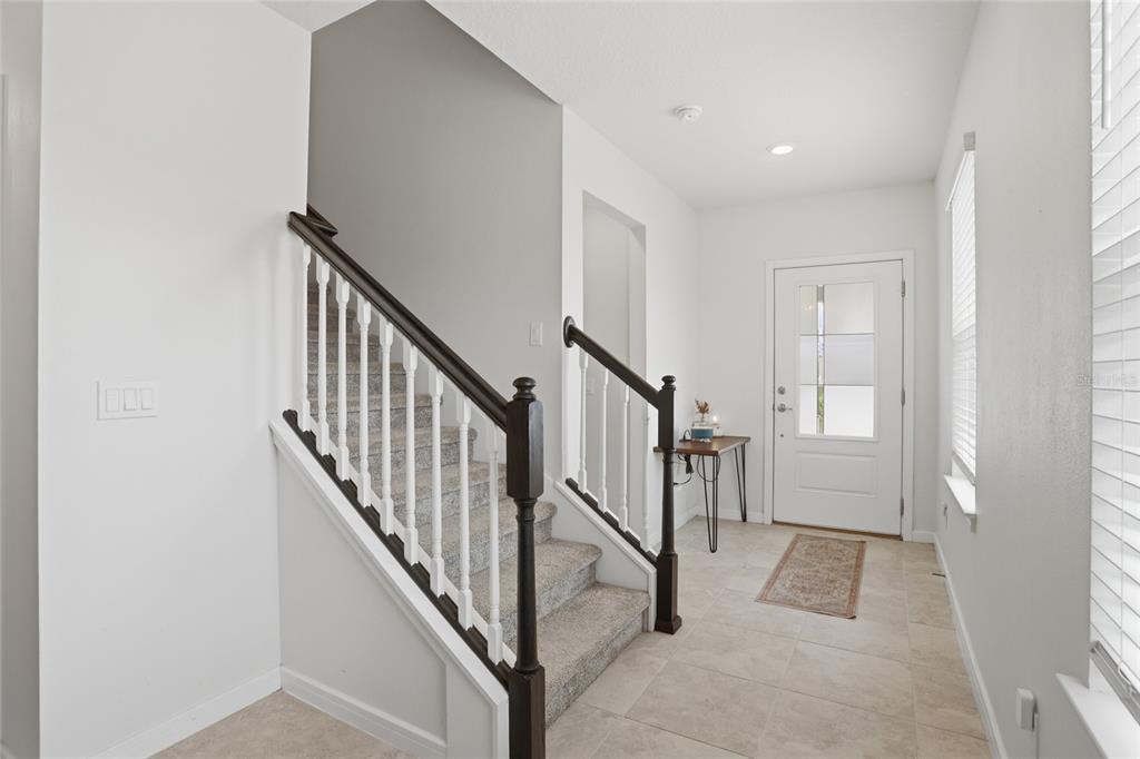An entryway features a carpeted staircase with dark wood railings and light tile flooring — 1818 GROVELINE ROAD, ST CLOUD, FL