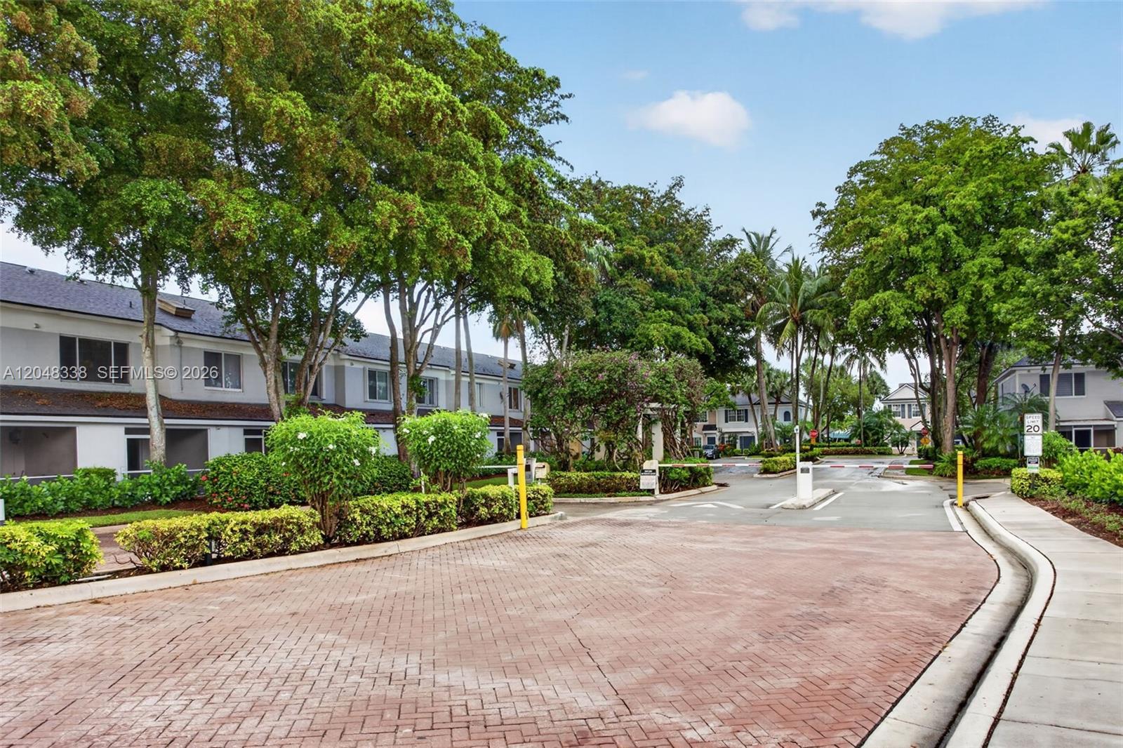 A paved driveway leads to a gated entrance surrounded by lush trees and residential buildings — 3364 Celebration Ln # 156, Margate FL 33063, MARGATE, FL
