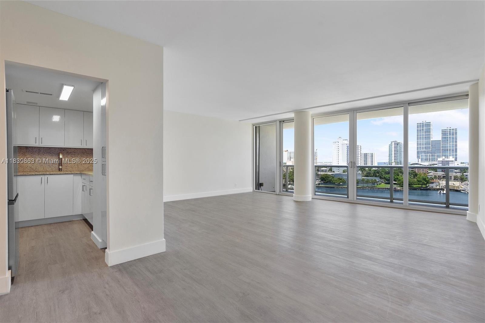 An open living area with light wood floors leads to a balcony overlooking a city skyline — 900 Bay Dr, Miami Beach FL 33141, MIAMI BEACH, FL