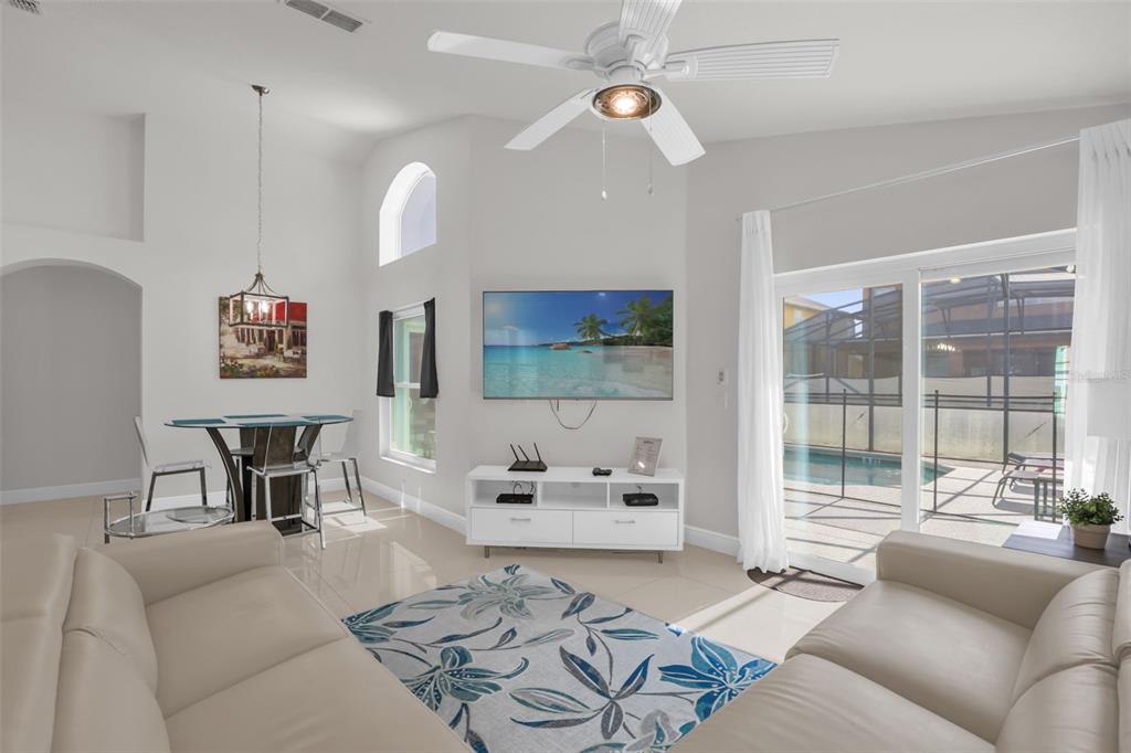 A living room with a ceiling fan, TV, white media console, and sliding doors to a pool — 156 BAREFOOT BEACH WAY, KISSIMMEE, FL