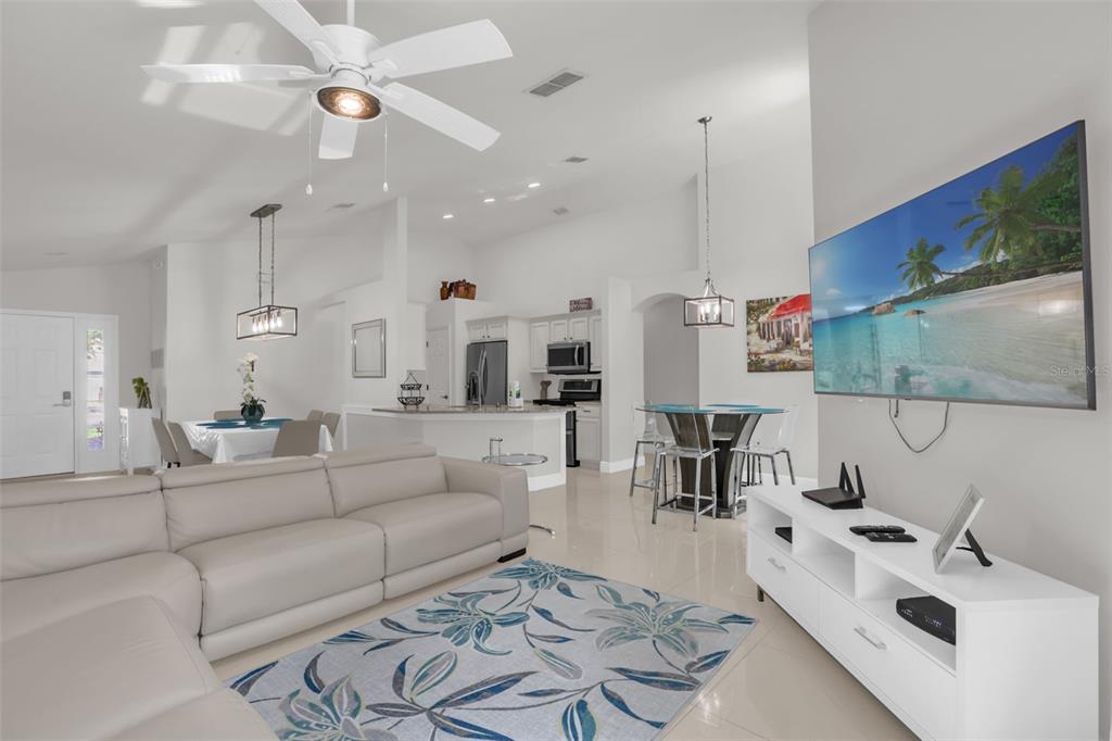 A living room with a white sectional sofa, a floral rug, and a wall-mounted television — 156 BAREFOOT BEACH WAY, KISSIMMEE, FL