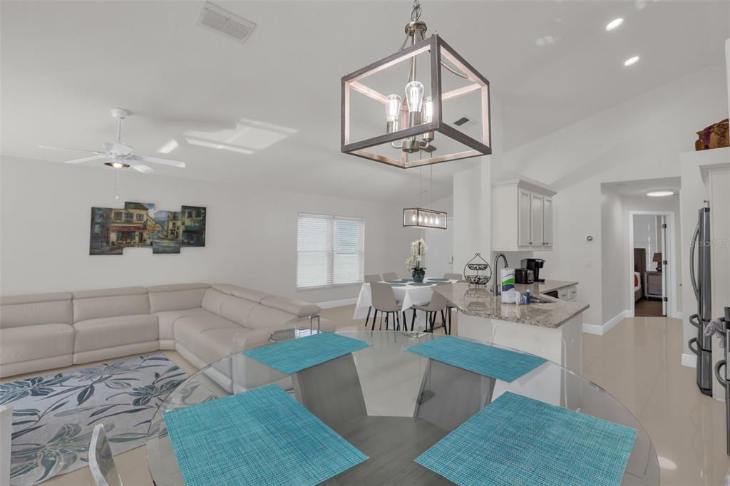 An open-concept living and dining area features a sectional sofa, kitchen island, and pendant lighting — 156 BAREFOOT BEACH WAY, KISSIMMEE, FL