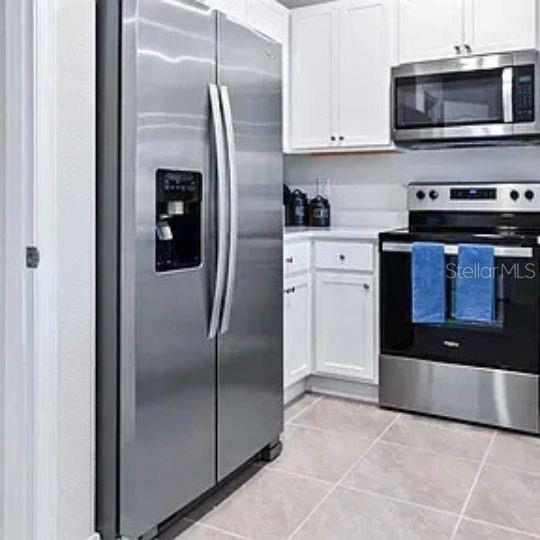 A kitchen features stainless steel appliances, white cabinets, and light-colored tile flooring — 4615 LINDA DRIVE, LAKE WALES, FL