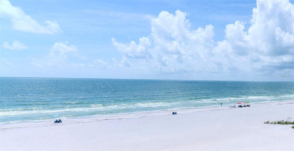 A wide, sandy beach meets the ocean under a bright blue sky with scattered clouds — 20040 GULF BOULEVARD UNIT 402, INDIAN ROCKS BEACH, FL