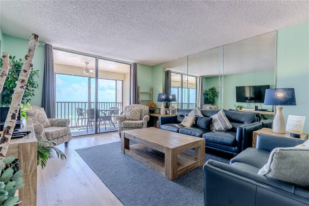 A living room features a blue leather sofa, wooden coffee table, and balcony ocean views — 20040 GULF BOULEVARD UNIT 402, INDIAN ROCKS BEACH, FL
