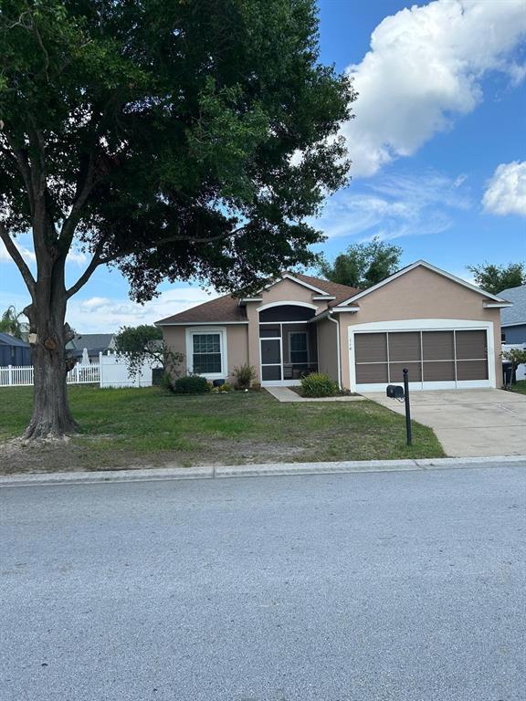 A single-story house with a tan stucco exterior, a screened front entryway, and a large tree — 110 KNOLLWOOD DRIVE, DAVENPORT, FL