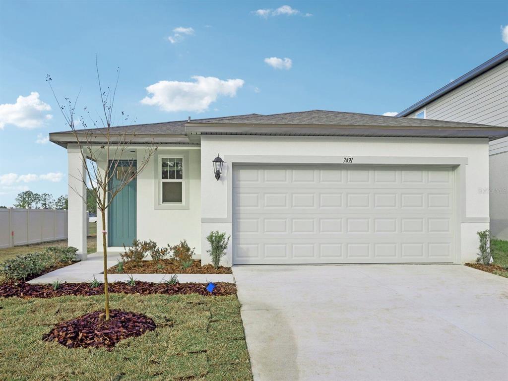 A single-story house with a white stucco exterior, a two-car garage, and a teal door — 7491 MIA VINE DRIVE, BROOKSVILLE, FL