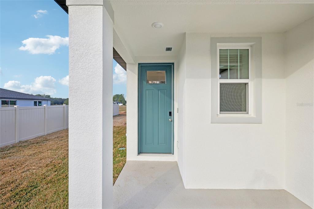 A covered entryway features a blue front door, a single window, and white stucco walls — 7491 MIA VINE DRIVE, BROOKSVILLE, FL