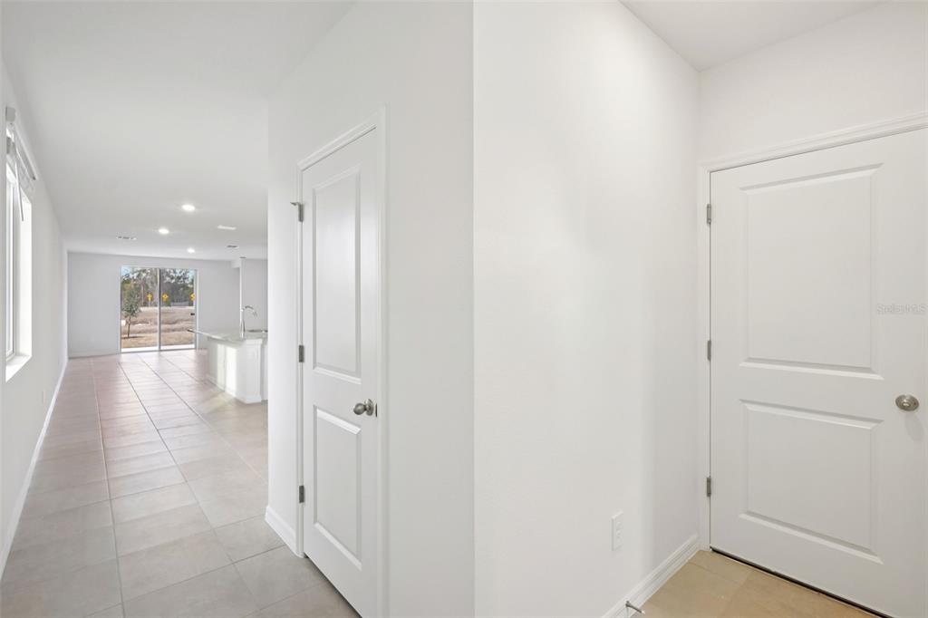 A hallway with white walls and tile flooring leads toward an open kitchen and living area — 7491 MIA VINE DRIVE, BROOKSVILLE, FL