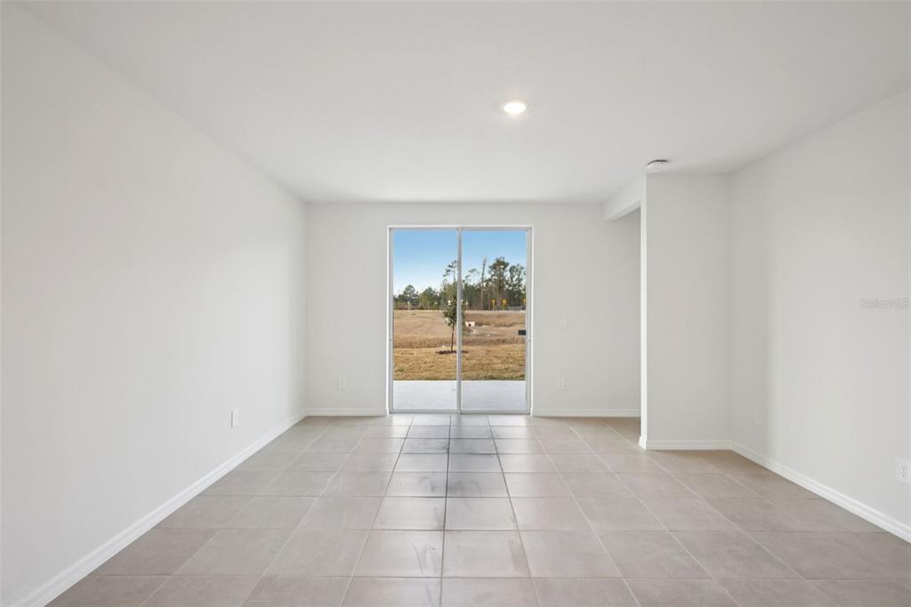 An empty room with light-colored tile flooring and a sliding glass door leading outside — 7491 MIA VINE DRIVE, BROOKSVILLE, FL
