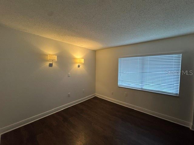 An empty room features dark wood-look flooring, two wall-mounted sconces, and a window with blinds — 4735 S TEXAS AVENUE UNIT 4735C, ORLANDO, FL