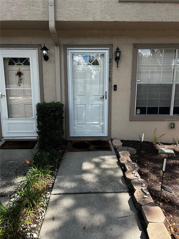 A concrete walkway leads to the front entrance of a tan townhouse with two doors — 2118 FLETCHERS POINT CIRCLE, TAMPA, FL