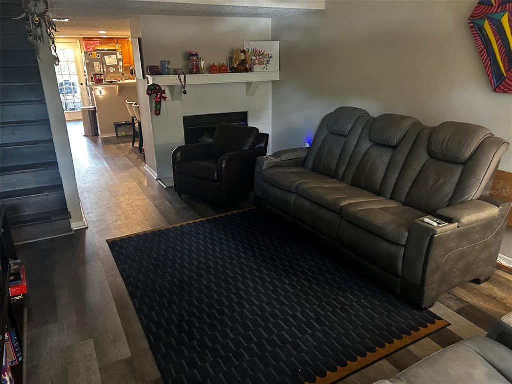 A living room features a grey reclining sofa, a dark armchair, a fireplace, and wood-look flooring — 2118 FLETCHERS POINT CIRCLE, TAMPA, FL
