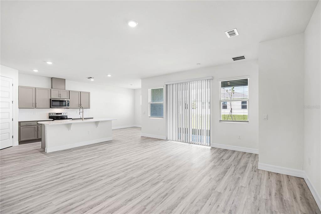 An open-concept kitchen and living area features light wood-look flooring and a sliding glass door — 5415 CLOUDBERRY AVENUE, LAKELAND, FL