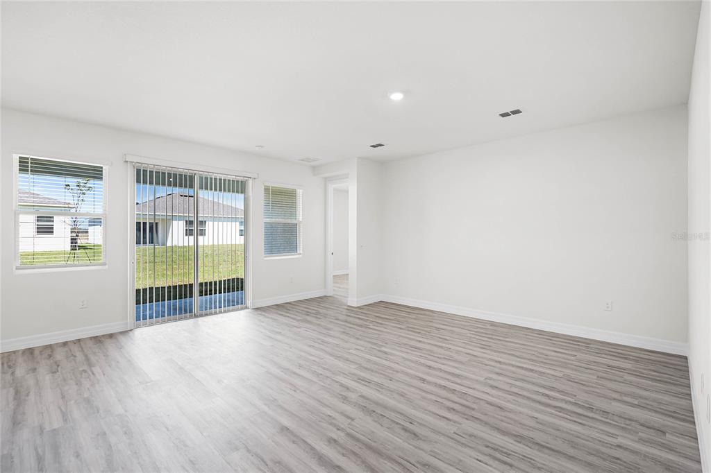 A bright living room features light wood-look flooring, white walls, and a sliding glass door — 5415 CLOUDBERRY AVENUE, LAKELAND, FL