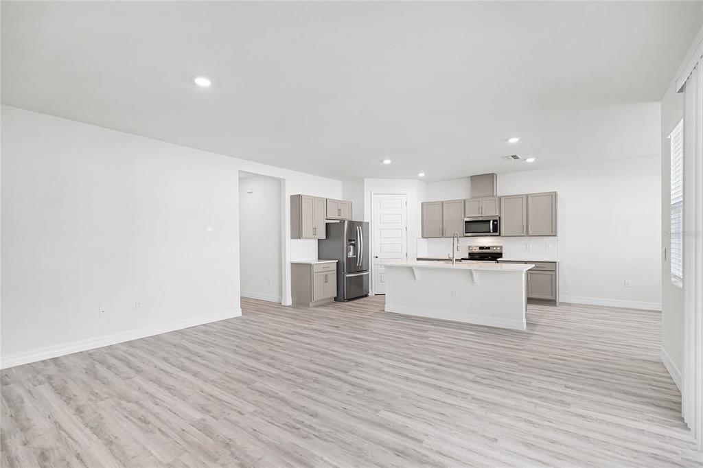 An open-concept kitchen features light gray cabinetry, a white island, and light wood-look flooring — 5415 CLOUDBERRY AVENUE, LAKELAND, FL