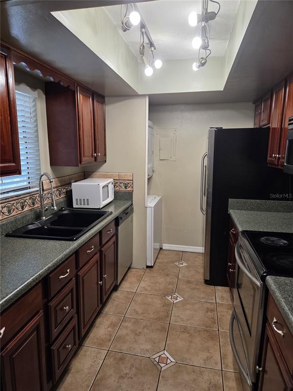 A galley kitchen features wood cabinets, dark countertops, a black sink, and stainless steel appliances — 4326 AQUA VISTA DRIVE UNIT 10E, ORLANDO, FL