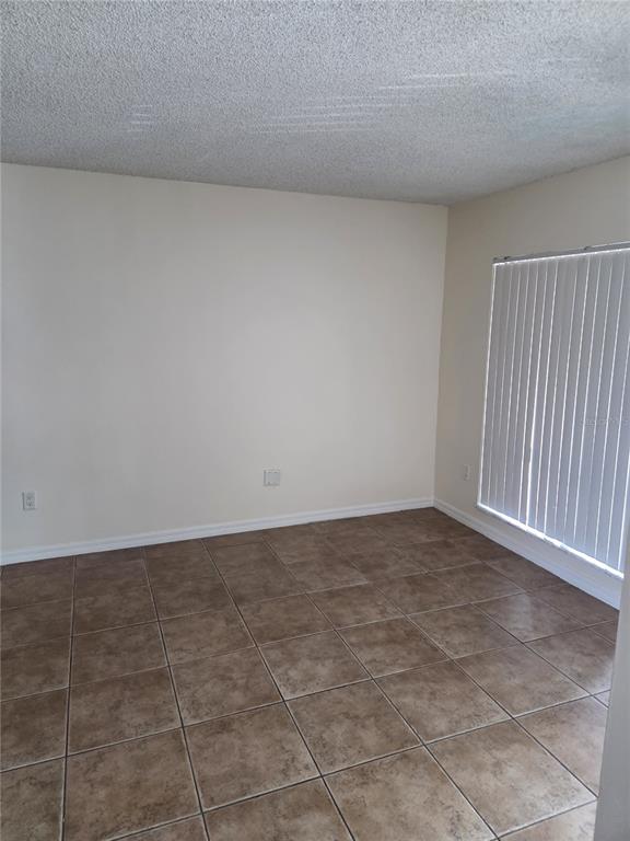 An empty room features beige walls, a textured ceiling, and brown square floor tiles — 4326 AQUA VISTA DRIVE UNIT 10E, ORLANDO, FL