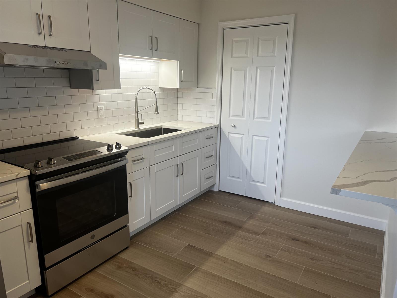 A kitchen features white cabinets, stainless steel appliances, a subway tile backsplash, and wood-look flooring — 609 NE 6th Court # B, Boynton Beach FL 33435, BOYNTON BEACH, FL