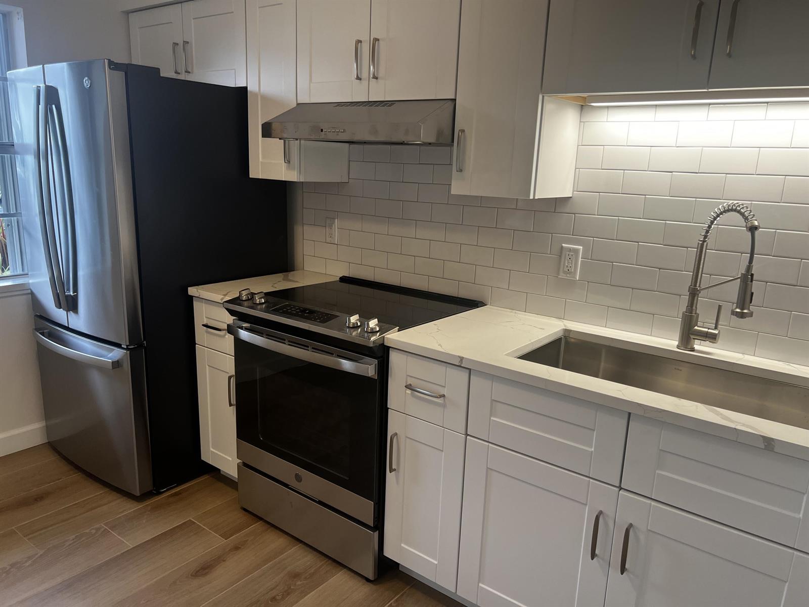 A modern kitchen features white cabinets, stainless steel appliances, subway tile backsplash, and quartz countertops — 609 NE 6th Court # B, Boynton Beach FL 33435, BOYNTON BEACH, FL