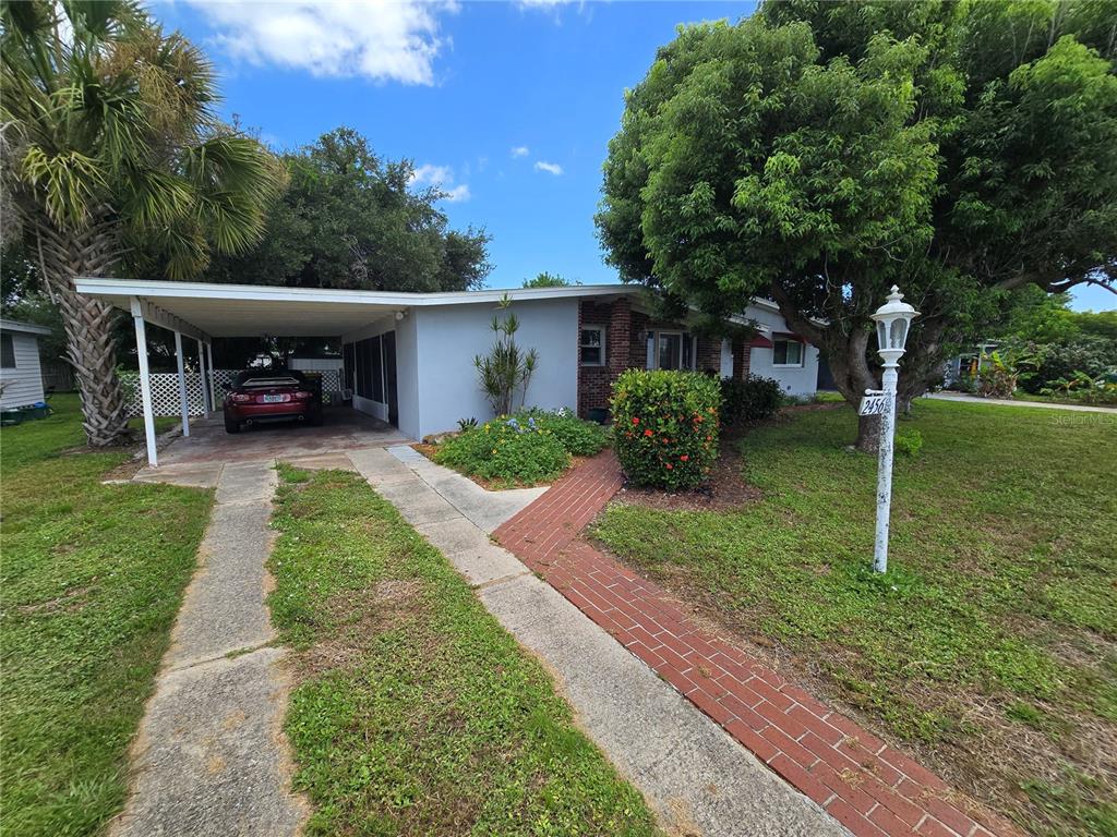 A single-story house features a carport, a brick walkway, and a prominent tree in front — 2456 EDNOR STREET, PORT CHARLOTTE, FL