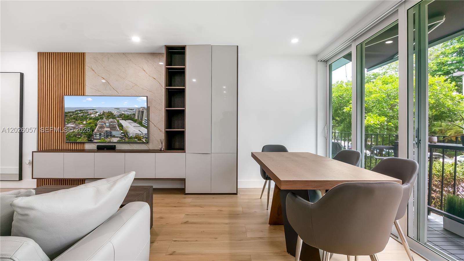 A modern living and dining room features a wood-slatted wall, marble accent, and balcony views — 2539 S Bayshore Dr # 212A, Miami FL 33133, MIAMI, FL