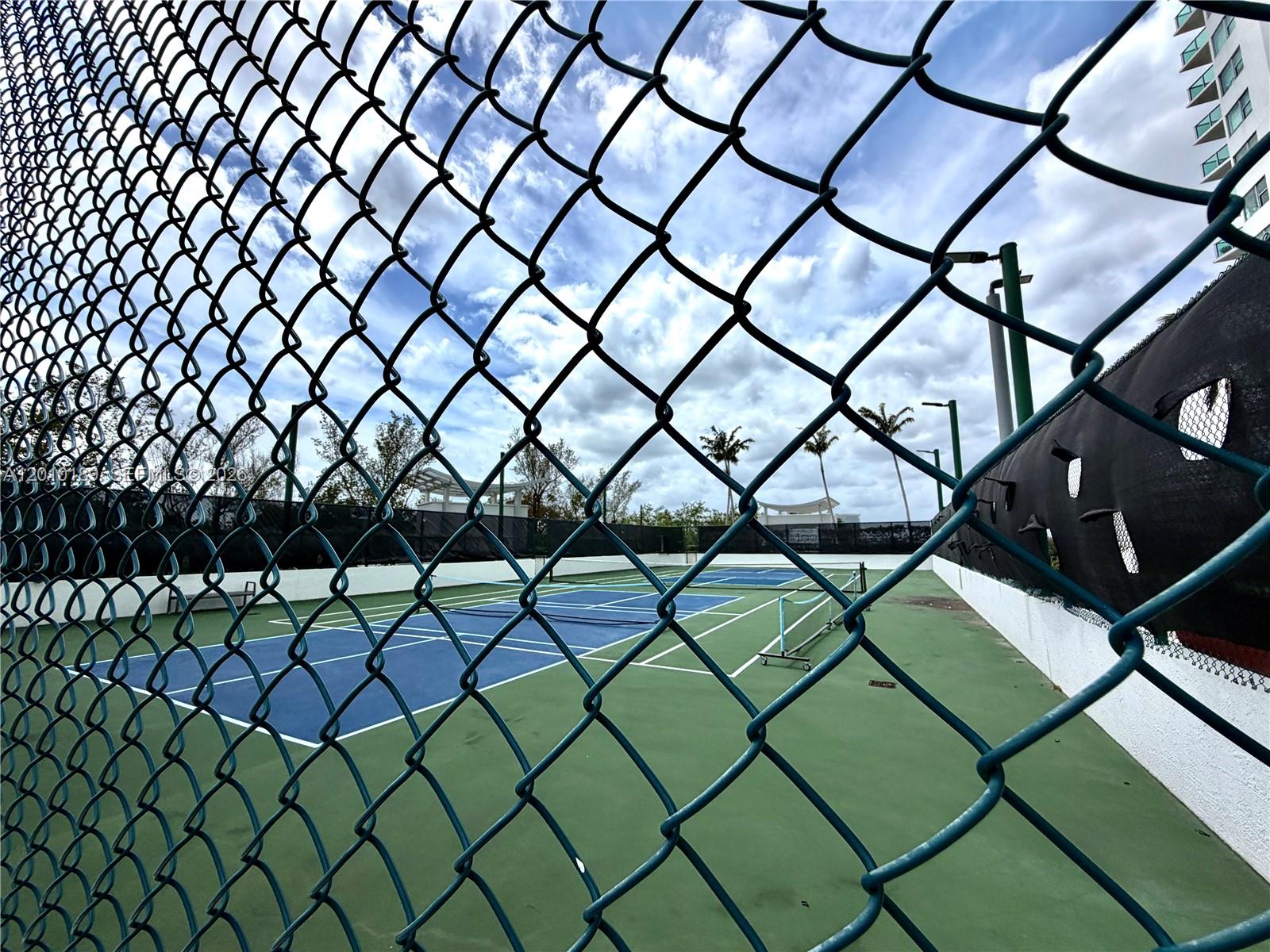 A chain-link fence overlooks a blue and green outdoor tennis court under a cloudy sky — 2641 N Flamingo Rd, Sunrise FL 33323, SUNRISE, FL