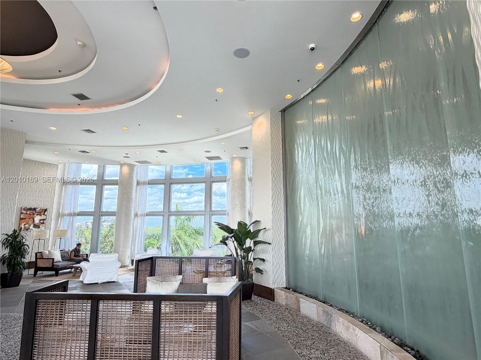 A modern lobby features a large indoor water wall, floor-to-ceiling windows, and lounge seating — 2641 N Flamingo Rd, Sunrise FL 33323, SUNRISE, FL