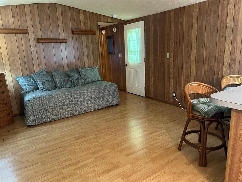 A room with wood-paneled walls, light wood flooring, a daybed, and a rattan chair — 12482 161ST ROAD, LIVE OAK, FL