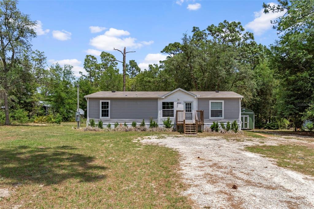A single-story manufactured home with grey siding sits on a gravel driveway in a wooded area — 2063 S SUNWOOD POINT, HOMOSASSA, FL