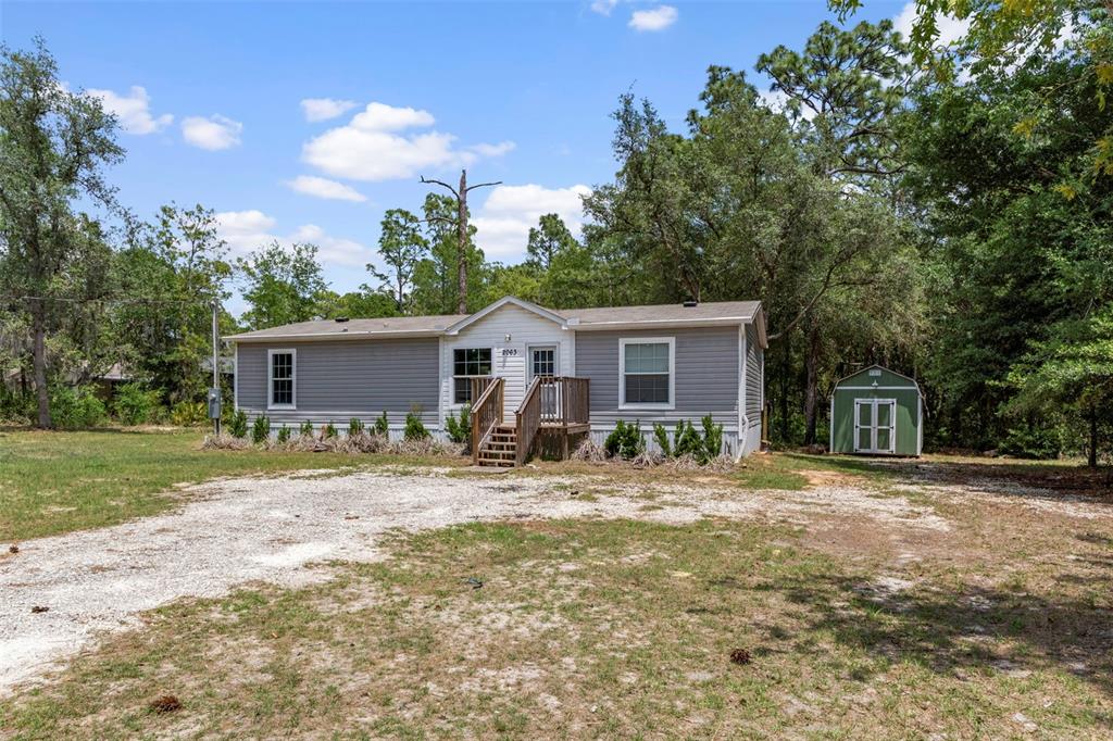 A single-story gray manufactured home with a wooden porch and a small green storage shed — 2063 S SUNWOOD POINT, HOMOSASSA, FL