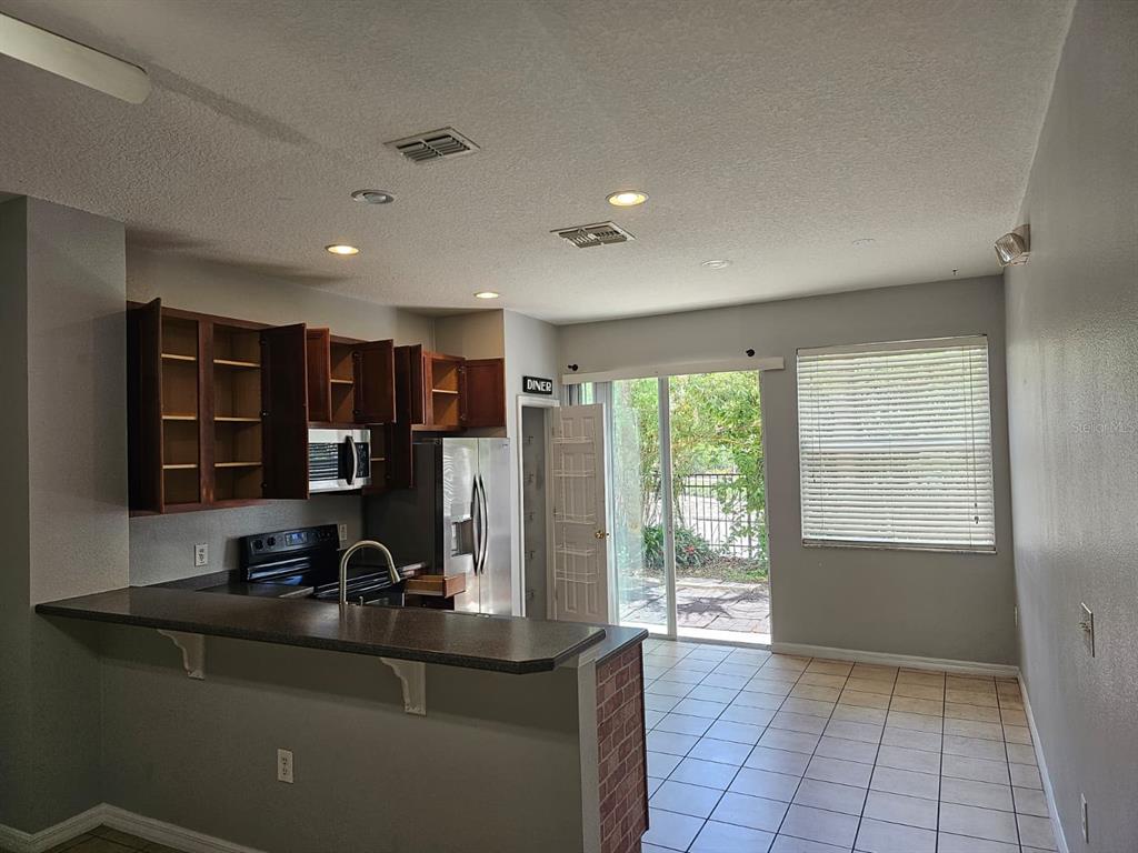 A kitchen with wood cabinets and a breakfast bar overlooks a tiled living area — 5116 DOMINICA DRIVE, KISSIMMEE, FL