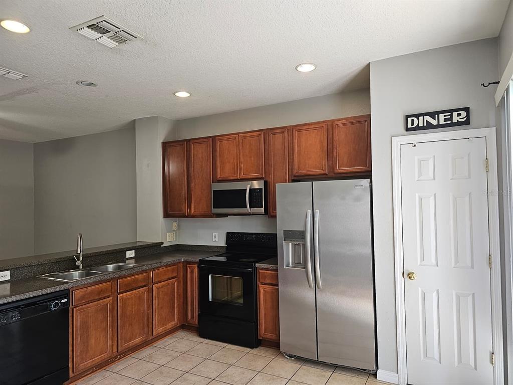 A kitchen with wood cabinets and a breakfast bar opens to a tiled dining area — 5116 DOMINICA DRIVE, KISSIMMEE, FL